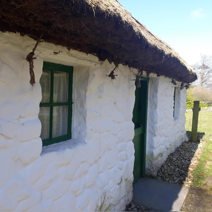 Thatched white house with two windows either side of a door. Window frames and door painted green.
