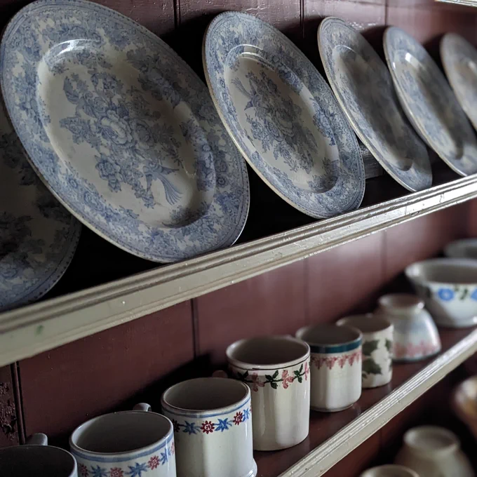 Brown dresser with cream edging. Blue and white patterned plates on top shelf. Mugs and bowls on shelves below.