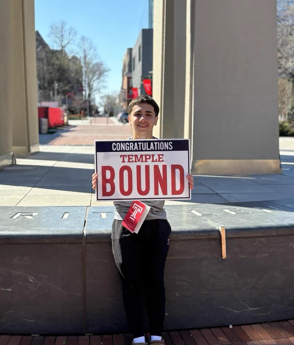 Future Temple student holding a 'Congratulations Temple Bound' sign at the Bell Tower. 