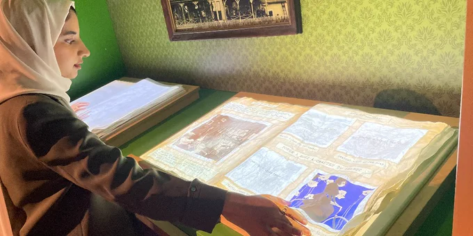 A young woman in a hijab examines an illuminated manuscript.
