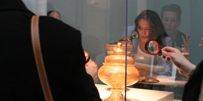 Three young women examine artifacts inside a display case using magnifying glasses.