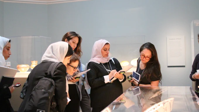 A group of women take notes while examining artifacts in a museum display case.