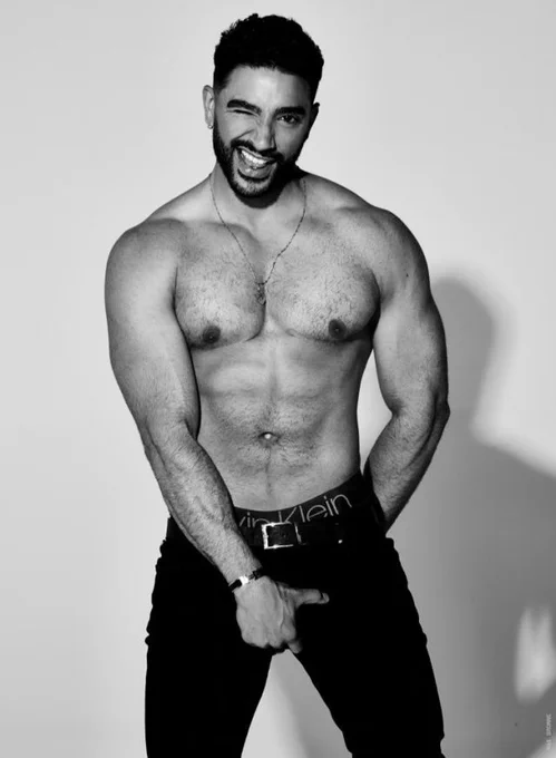 Black and white photo of Laith Ashley posing shirtless. Dark haired and brown eyed muscular man with a full beard