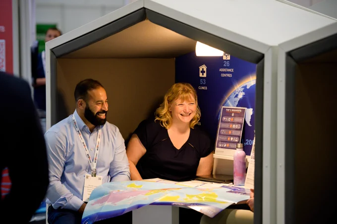 Photo of a man and woman sat inside a white Nook pod with grey interiors. They're both laughing at something the person opposite them has said. 