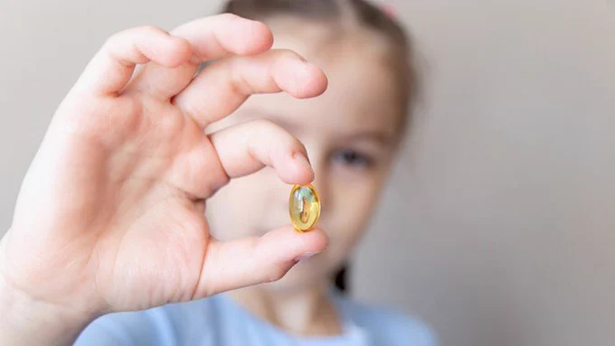 A child holding up an omega-3 supplement.