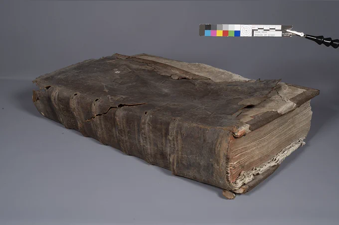 A tattered and torn brown book with worn pages, closed and showing the front cover and spine.