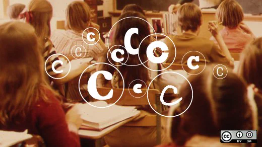 A group of young students photographed from the back, facing forward in a classroom. A blackboard and a stading teacher's hand just visible. Copyright symbols superimposed on the image. Image licence icon on the bottom right (CC BY SA).