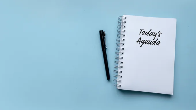 ‘Today’s Agenda’ written in black ink on a spiral-bound notebook next to a black pen. The background is pale blue. Image by Faizal Ramli via Shutterstock.