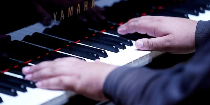 A close-up of a person playing a Yamaha piano. 
