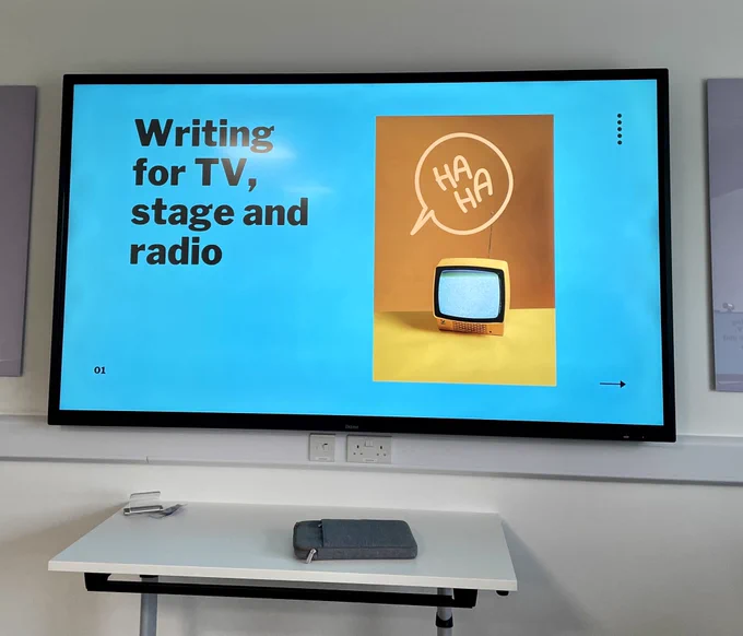 Presentation screen in a classroom. Slide reads ‘Writing for TV, stage and radio.’ There’s an image of a TV, with the words ‘HA HA’ in a speech bubble alongside.