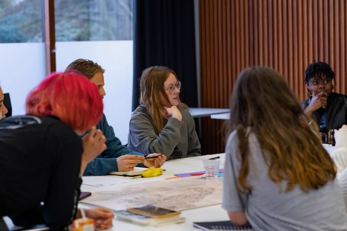 A group of young people sat around a table with writing supplies