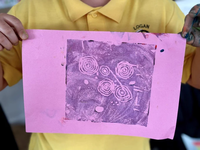 Photo of a pupil holding a print on pink paper. The print depicts cup and ring marks.