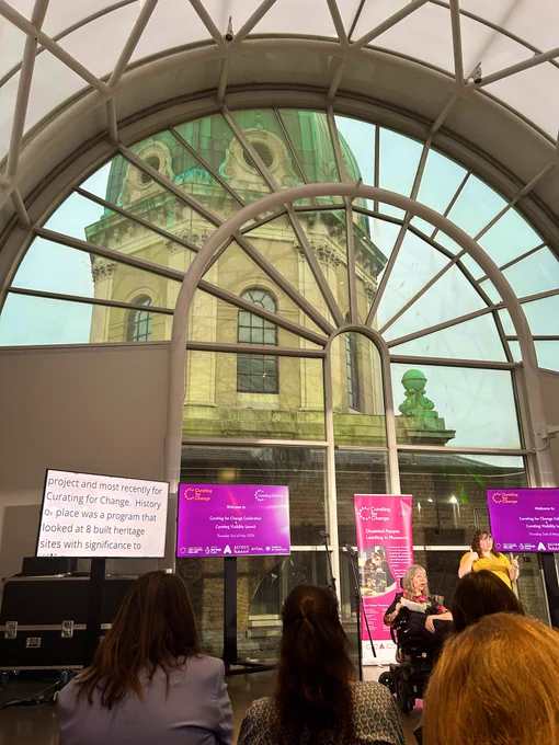 Esther Fox delivers a speech about the curating for change programme in front of large arched window