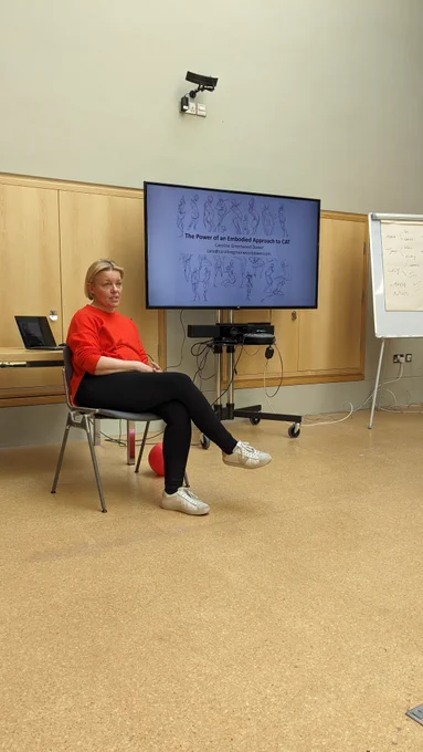 Caroline Greenwood Dower sitting in front of a screen introducing her talk on 'the power of an embodied approach to CAT'  at the Burrell Collection, CAT Scotland AGM & CPD day, April 2024