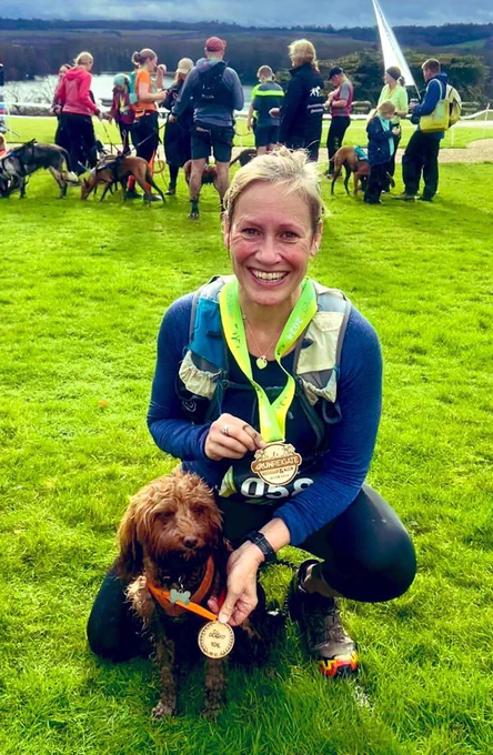 Lady and dog pose with running medals on a field.