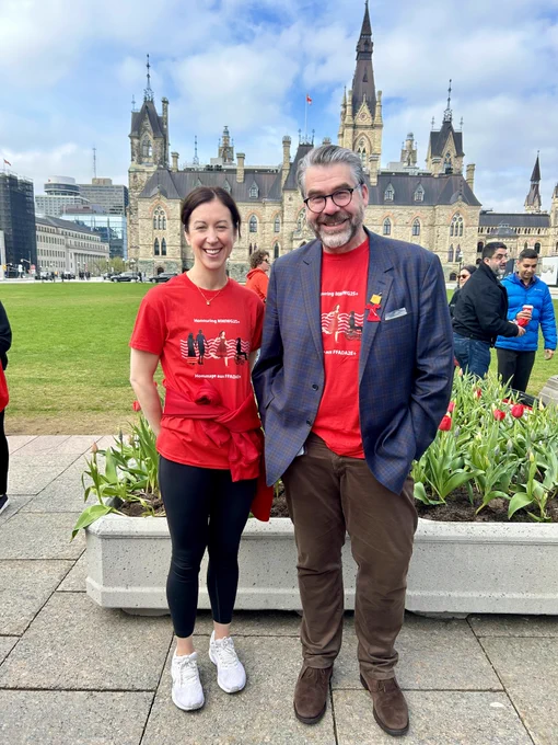 Clerk Hannaford and Deputy Clerk Fox standing next to each other on Parliament Hill each wearing a Movement is Medicine t-shirt. 