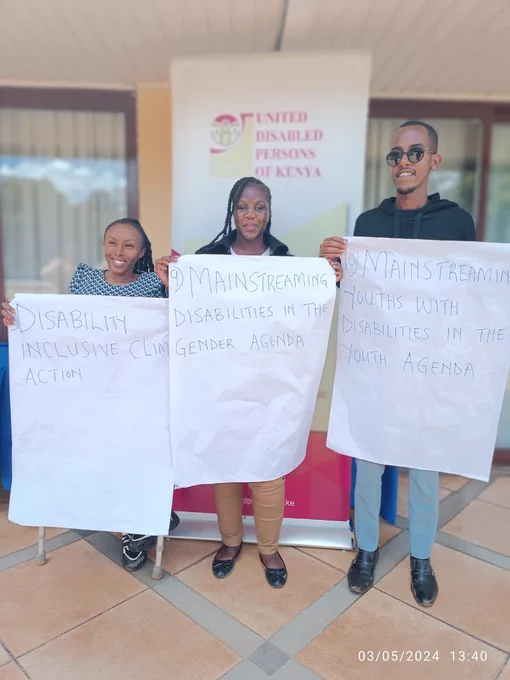 Three people standing in front of a banner. They are holding paper banners. 