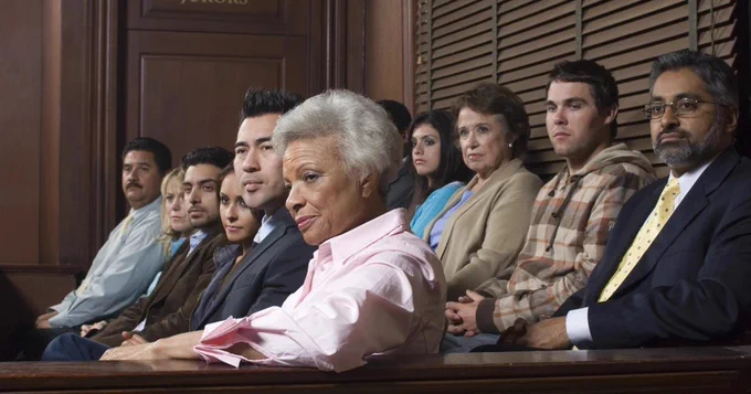 Eleven jurors are visible, sat in a courtroom watching the proceedings of a trial.