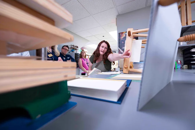 A Notre Dame Preservation employee points to an item on a table while two library employees look on.