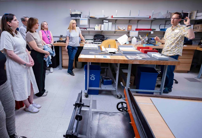Notre Dame Preservation employee on the right gestures while speaking to several library employees on the left. A large work table sits between them.