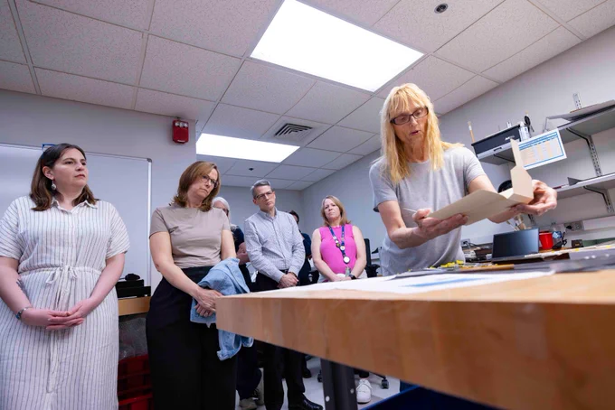 A Notre Dame Preservation employee on the right holds a folded box over a work table while speaking to library employees behind and on the left.