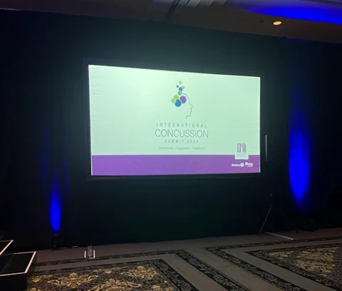 International Concussion Summit welcome slide projected on a large screen at the front of a hotel ballroom.