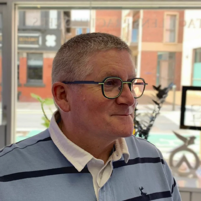 A gentleman with short hair wearing a black spectacle frame with a green coloured highlight ring around the entire lens and with a little injection of colour creeping down the side of the frame.