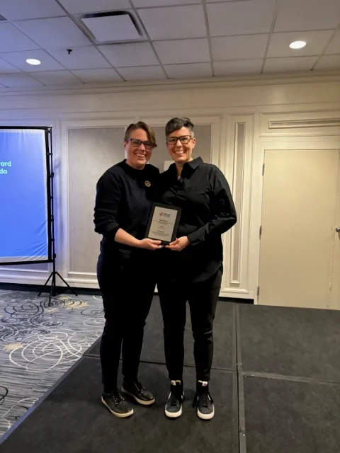 PHE Canada Board President, Jo Sheppard presenting PHE Canada 23-24 Impact Award to Ophea. Ophea Director of Partnerships and Public Affairs, Tammy Shubat is accepting the award on behalf of Ophea and is posing for a photo with Jo Sheppard as they both hold the plaque at the 2024 PHE National Conference awards ceremony. 
