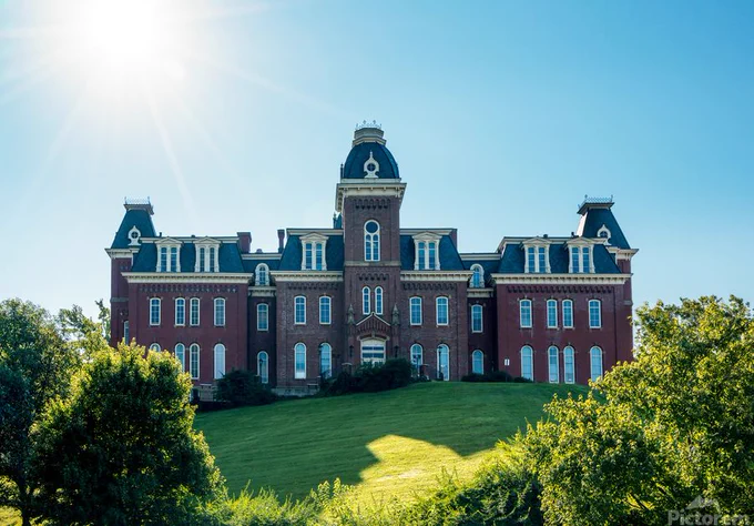 Rear view of Woodburn Hall at West Virginia University or WVU in Morgantown WV with a sunburst in the blue sky behind the building.