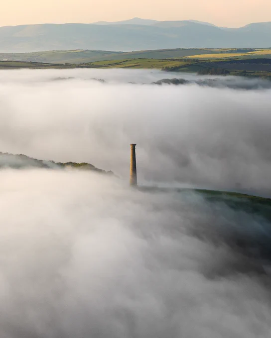 An aerial photograph of the wellington monument on top of Pen Dinas in Aberystwyth surrounded by a sea mist. The mountains of north wales can be seen on the horizon