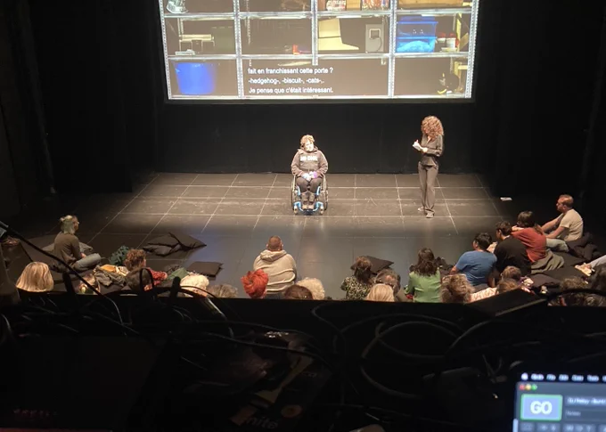 Jess Thom and Rossella Mezzina on stage with the audience shown at the bottom of the image and the screen at the back.