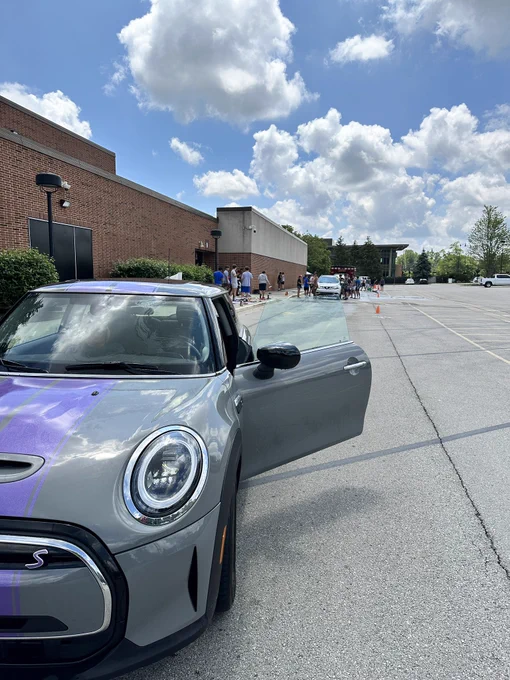 Silver Mini Cooper with a purple stripe in front of cars lined up to be washed by Carmel Football players at Carmel High School