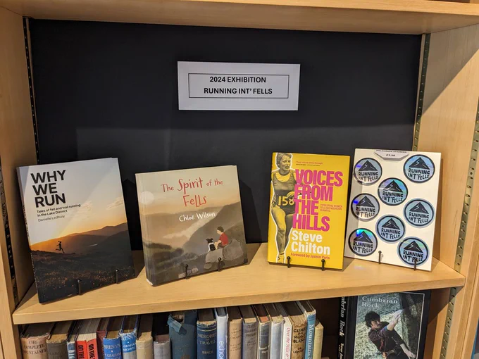 Three books on running and a sheet of holographic stickers of the black Running Int Fells logo. On the left is Why We Run by Danielle Ledbury. In the middle is The Spirit of the Fells by Chloe Wilson. On the right, next to the stickers, is Voices From The Fells by Steve Chilton