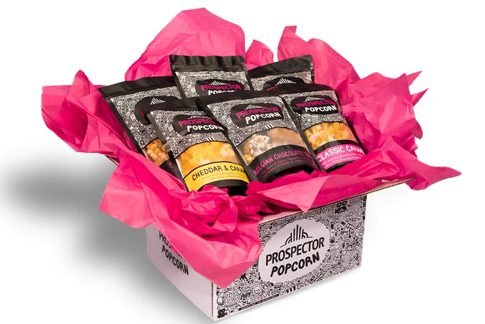 A box filled with different gourmet popcorn flavors sits on a white background.