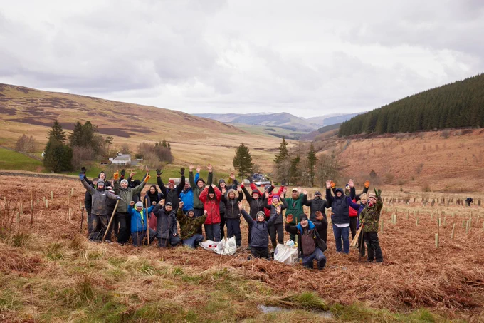 A group of volunteers cheer and raise their arms in a wild place where they have been planting trees. 