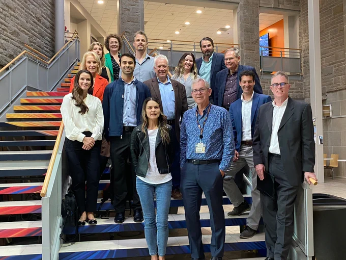 Members of Queen's, Kingston Health Sciences Centre, Kingston Economic Development and SUNY Medical stand on a staircase in the Queen's Biosciences Complex