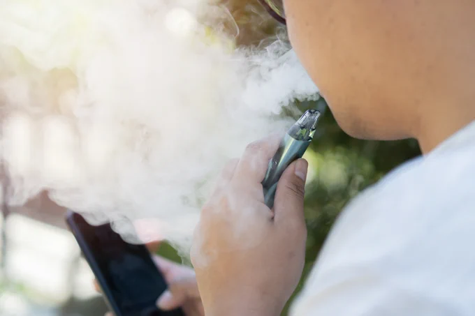 Photo of someone using a vaping device and holding a phone.