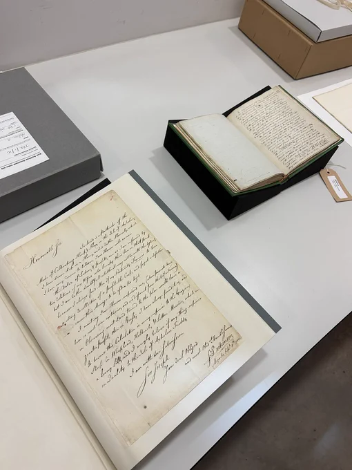White table with two archival documents open on it. Both have beautiful cursive handwriting on display on the pages.