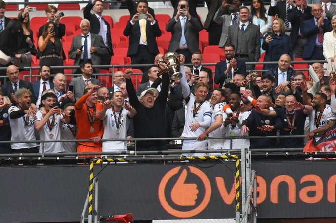 Photo of Bromley FC players and manager celebrating with the trophy in the stands at Wembley.
