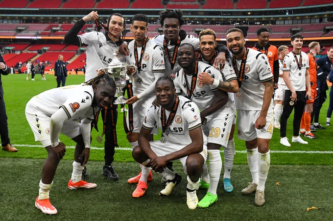 Photo of Bromley FC players celebrating with the trophy on the pitch at Wembley.