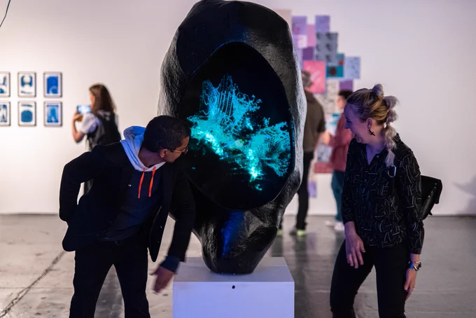 Image shows a 3D artwork of a large sculpture representing a cell with a projection within in representing DNA. The artwork is in a gallery setting and visitors are looking at and interacting with the work. Image is the property of SMQB and should not be reused or repurposed without permission, image credit: Hayley Salter.