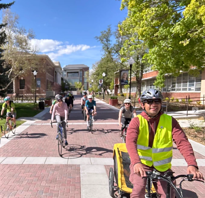 about 10 riders riding along a wide treel-lined path on the University of Nevada, Reno campus