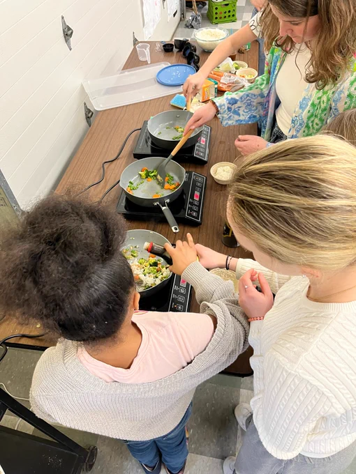 High angle view of 4 youth preparing food in skillets on hot plates.