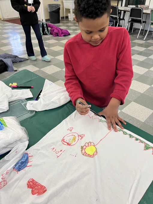 A 4-H youth member drawing a flower, cloud, and more on a t-shirt.