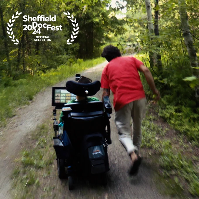 A motion blur photo of the back of Samuel and Isaiah on a wooded trail with Isaiah holding onto Samuel’s wheelchair running.