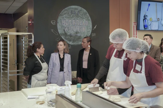 Speaker Adams speaking to two women while touring a kitchen. There are two students near her that are baking