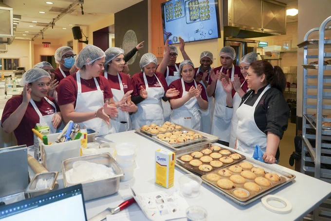 Culinary students standing around a table cheering and clapping while looking at trays of muffins they just baked 