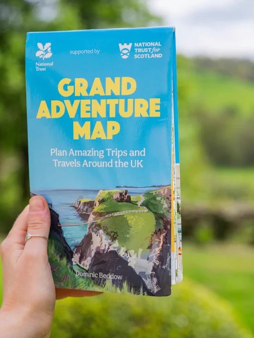 a person holding a folded map. The cover includes logos for both the National Trust and The National Trust for Scotland. Bold yellow text reads Grand Adventure Map followed by smaller sub title ' Plan Amazing Trips and Travels Around the UK'