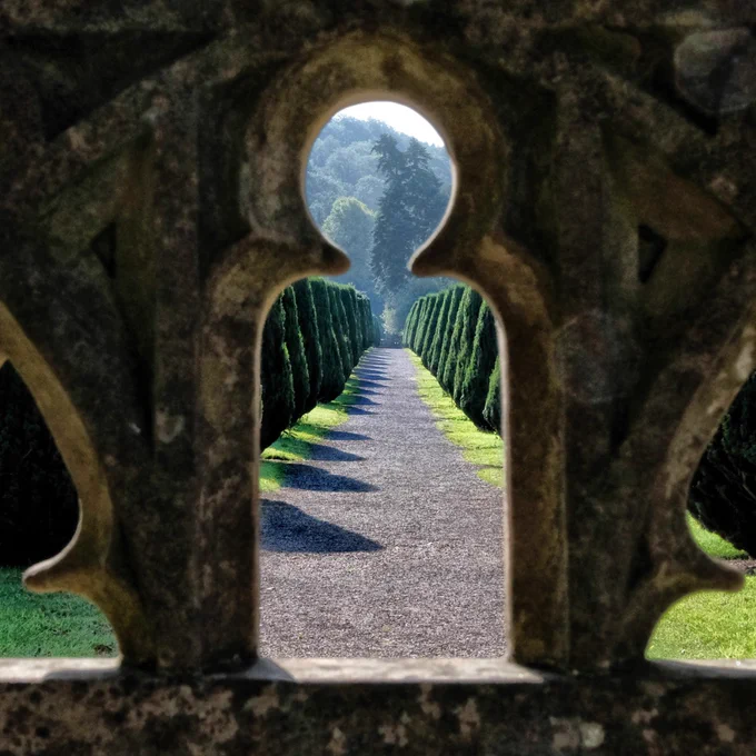 a view through a stone balustrade taking in a long path lined with trees. 