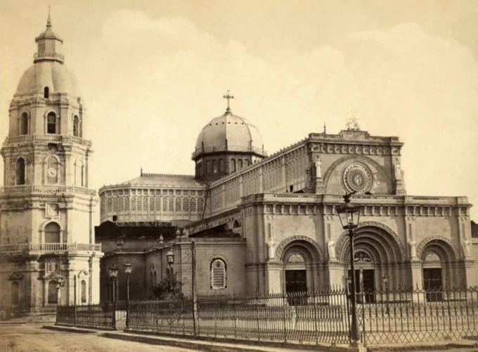 The cathedral of Manila, rebuilt after an earthquake, a huge cathedral building in basilica style with prominent romanesque doorways on the west façade, a small dome above the crossing and a freestanding bell tower with baroque pilasters